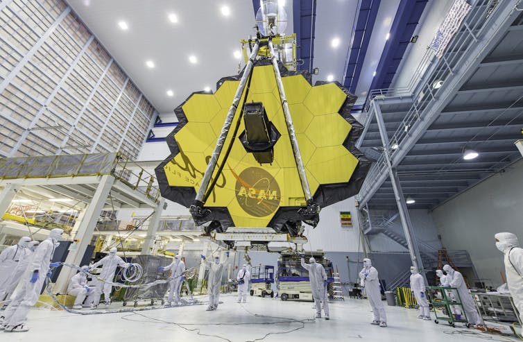 A large golden colored disc with a sensor in the middle and scientists standing below.